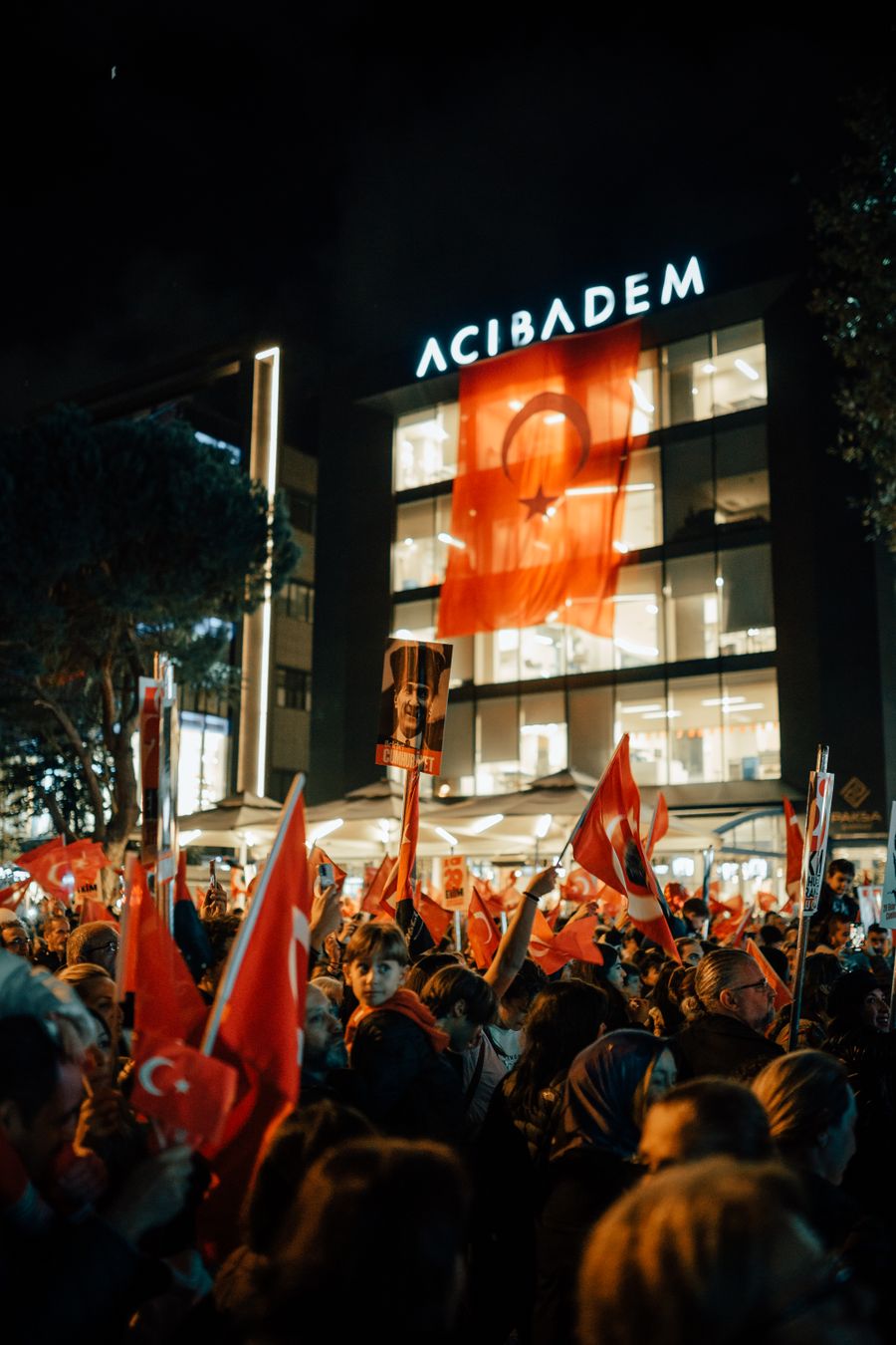 Gece ışıklı bir binanın önünde Türk bayraklarıyla toplanan kalabalık