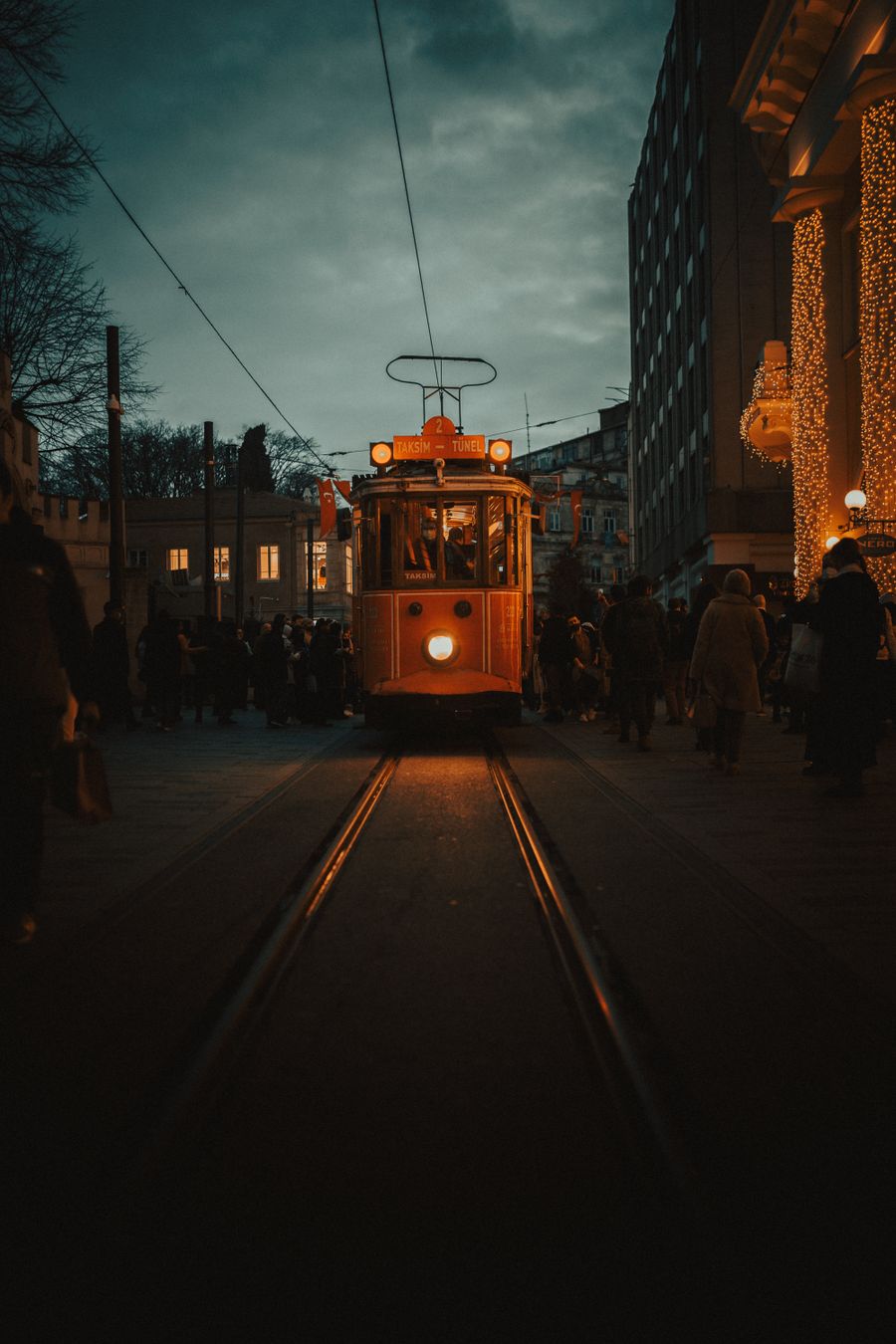 Alacakaranlıkta kalabalık bir caddede nostaljik tramvay