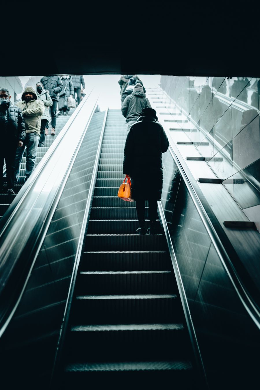 Metroda yürüyen merdivenle yukarı çıkan, turuncu çantalı biri