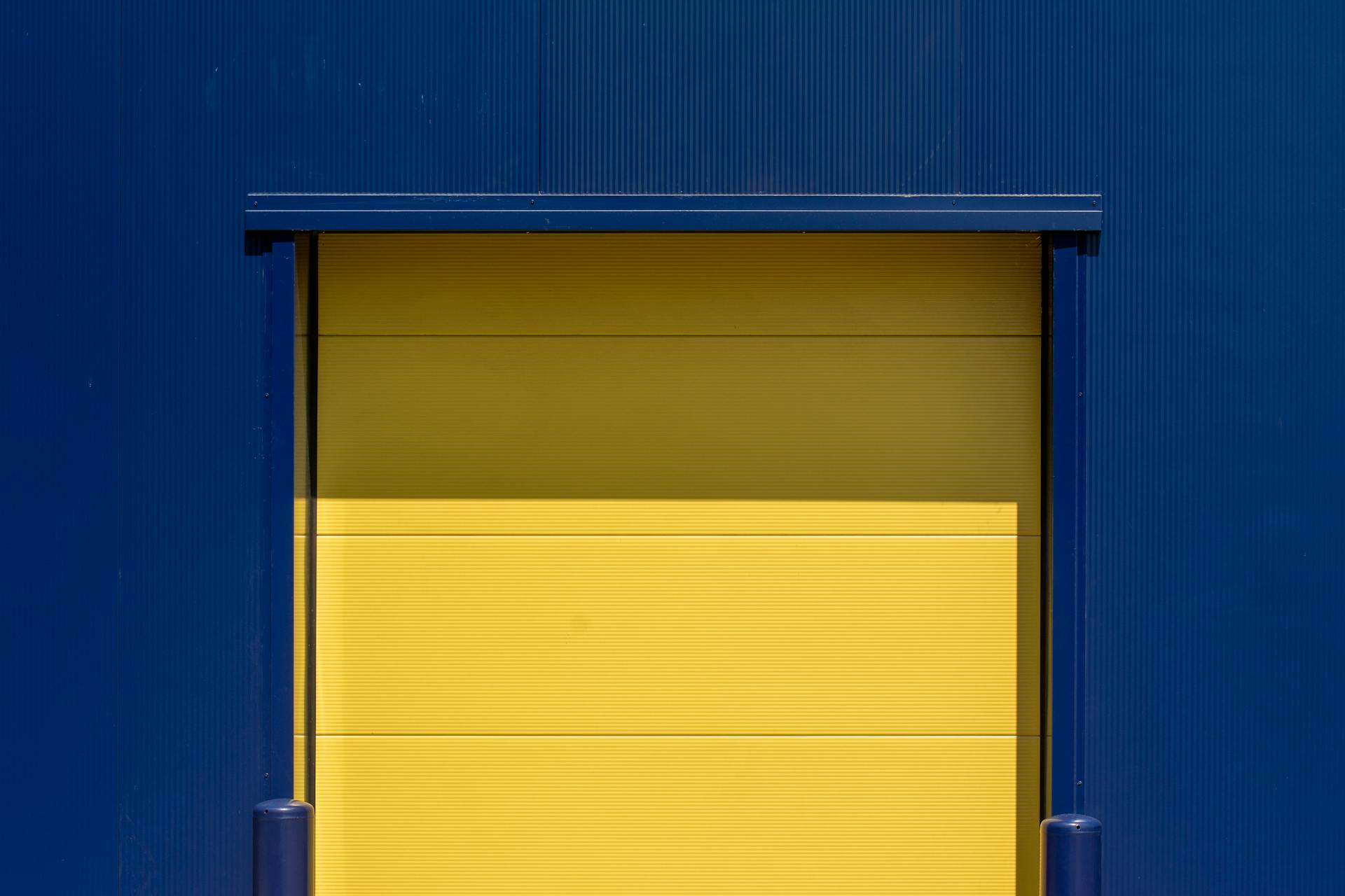 Vibrant yellow industrial door set against a blue metal wall, showcasing modern urban design.