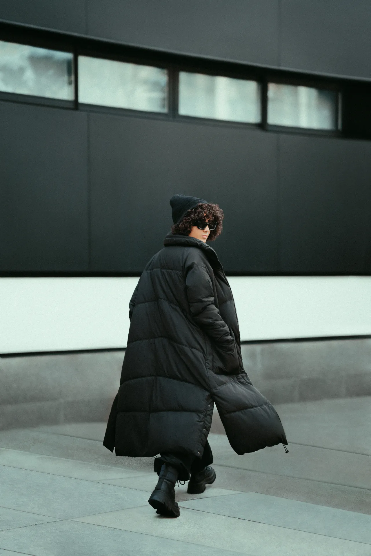 puffer-coat-winter-airport-outfit Woman in a long black puffer coat with beanie and sunglasses, a warm winter airport outfit