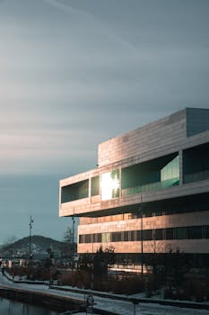 A contemporary glass building in Oslo reflecting sunset light, outdoors.