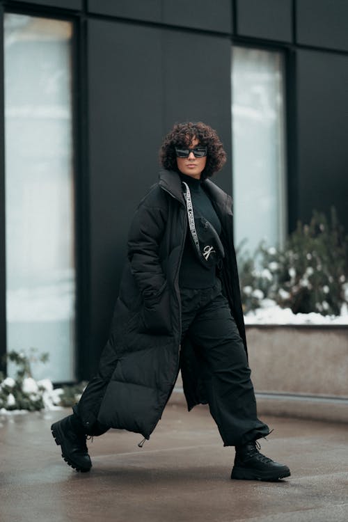 Free Woman in a Winter Coat and Sunglasses Walking Down the Sidewalk Stock Photo