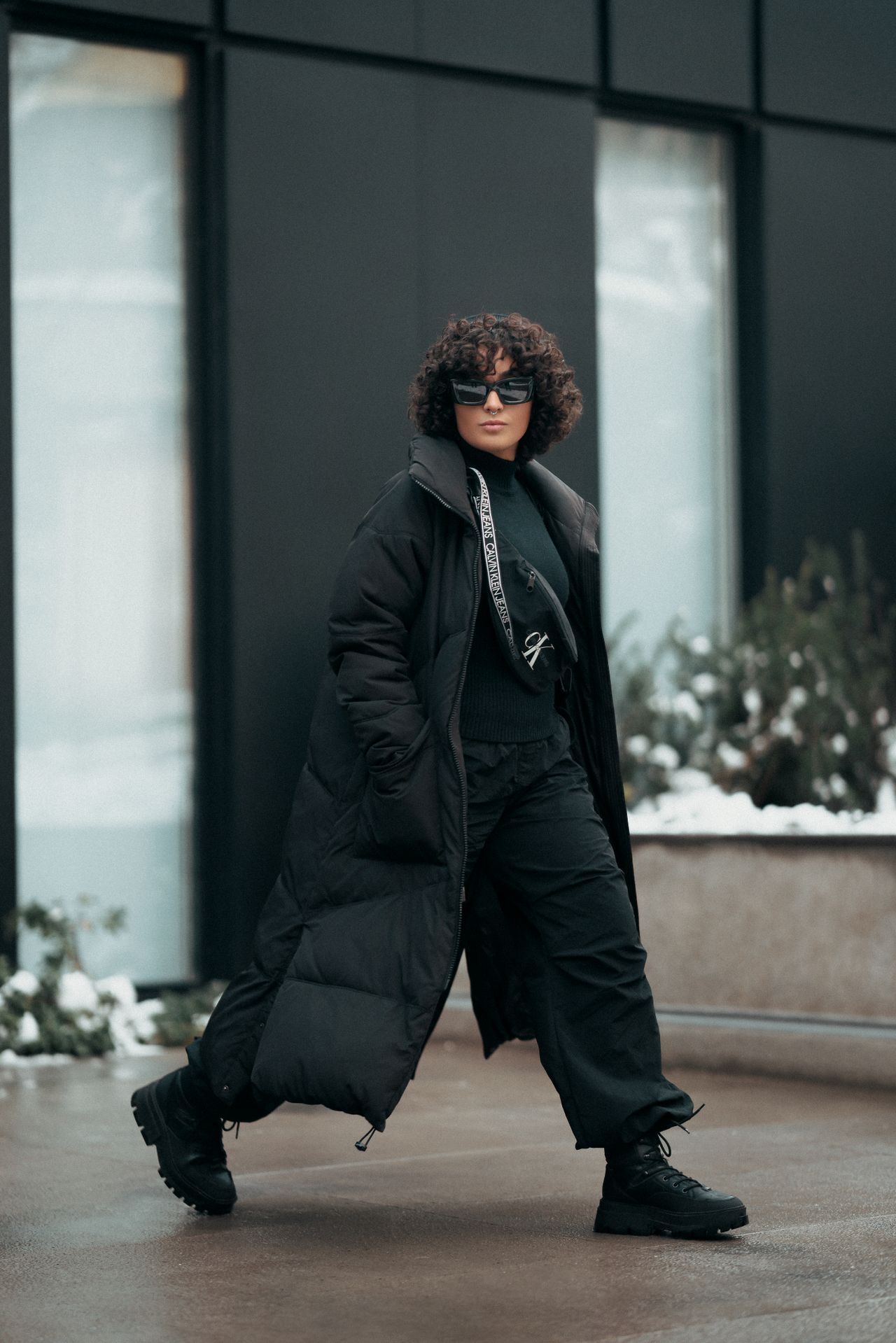 Woman bundled for a cold outdoor concert in a long black puffer coat, cargo pants and chunky boots in the snow