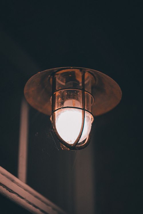 Free A glowing light bulb inside a vintage lantern, creating a warm ambiance against the dark backdrop. Stock Photo