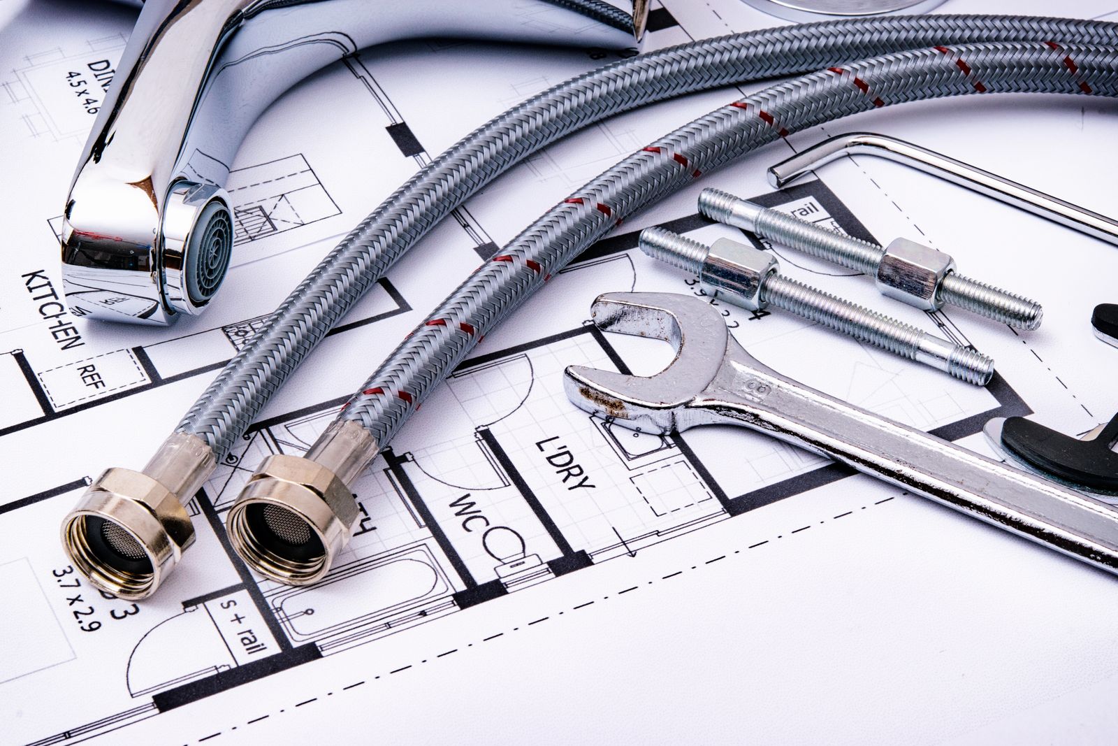 Plumbing tools and a faucet resting on an architectural drawing