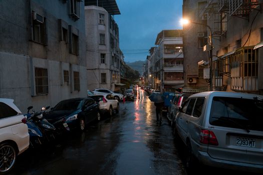 Moody urban street during a rainy night with reflections, parked cars, and streetlights.