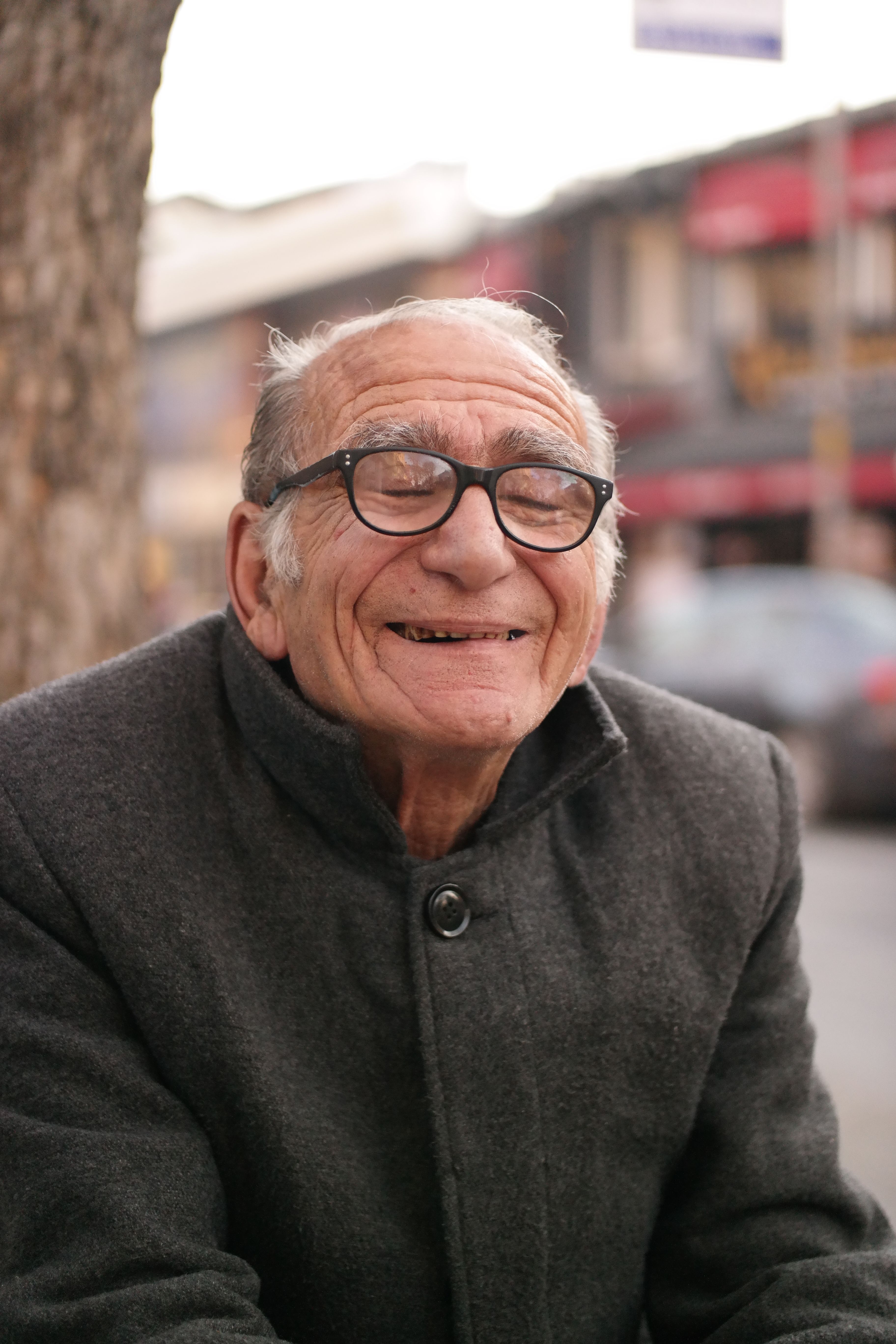 Charming portrait of a smiling elderly man with eyeglasses wearing a coat, outdoors.
