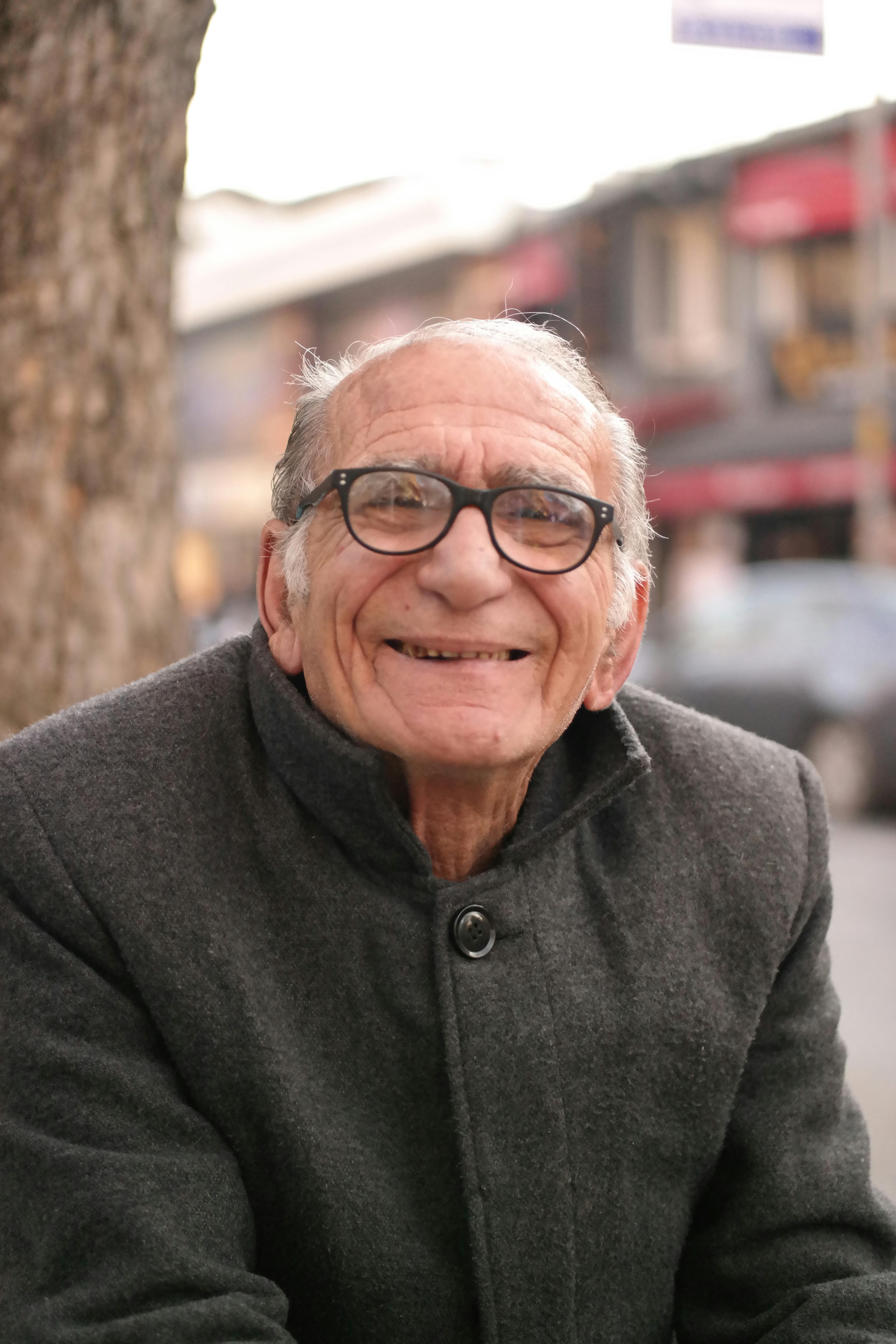 Portrait of a smiling elderly man outdoors, wearing a warm gray coat, suggesting a chilly day.