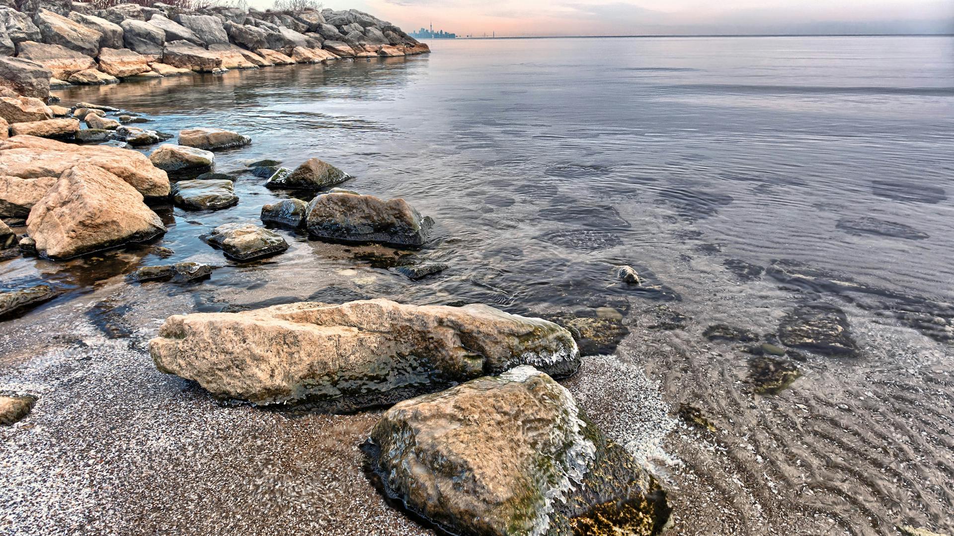 Peaceful shoreline in Mississauga, Ontario, showcasing rocks and calm water at dusk.