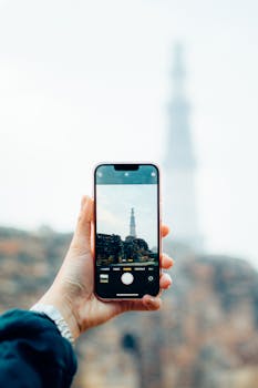 A hand holding a smartphone capturing the majestic Qutb Minar in focus with blurred background.