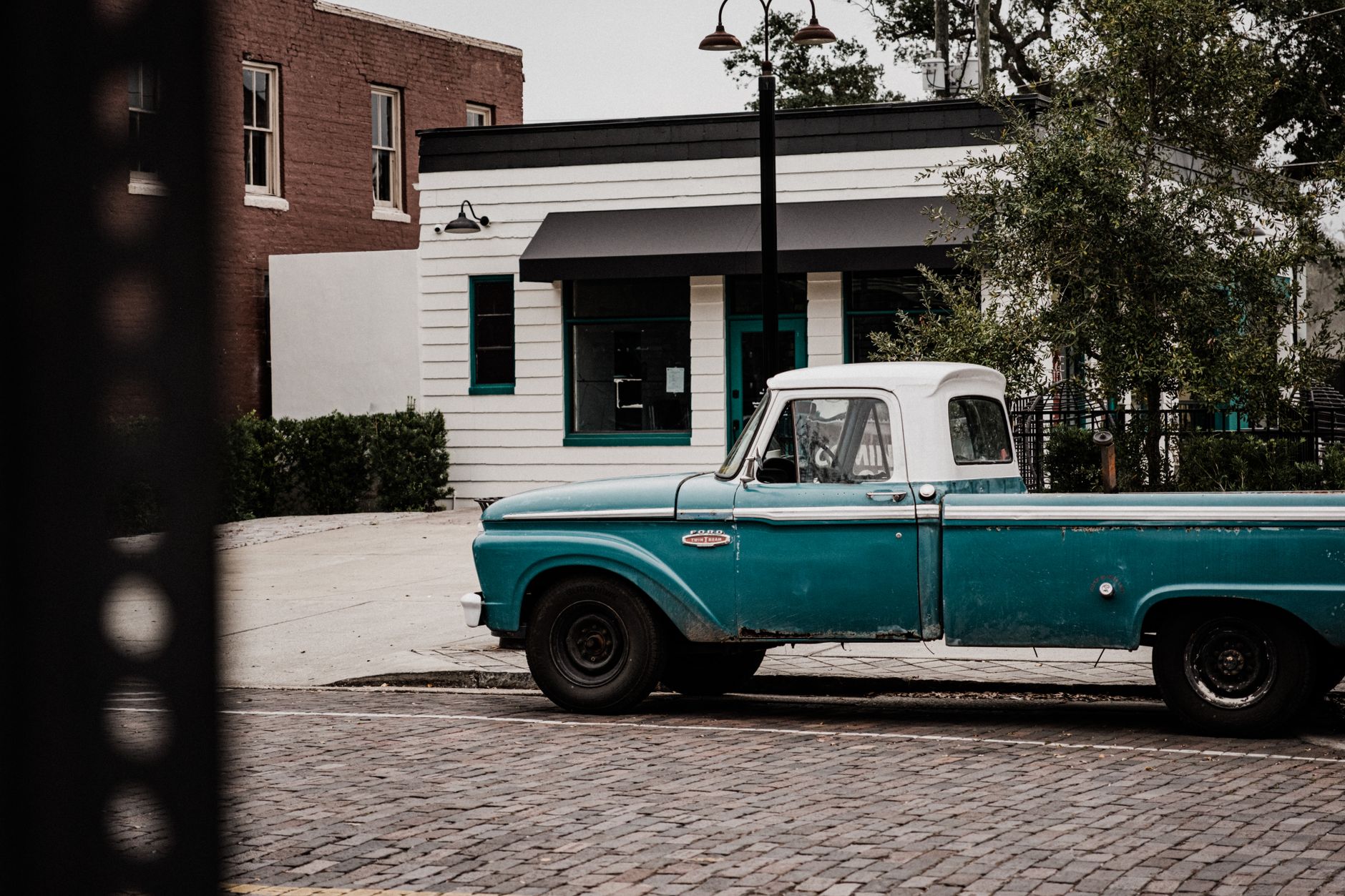 Classic blue pickup truck parked on a cobblestone street in front of vintage buildings.