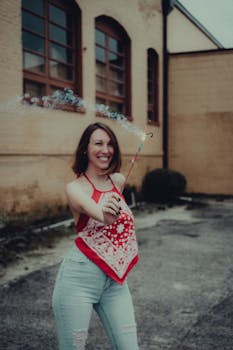 Cheerful woman in bright outfit holding a sparkler in an urban environment.