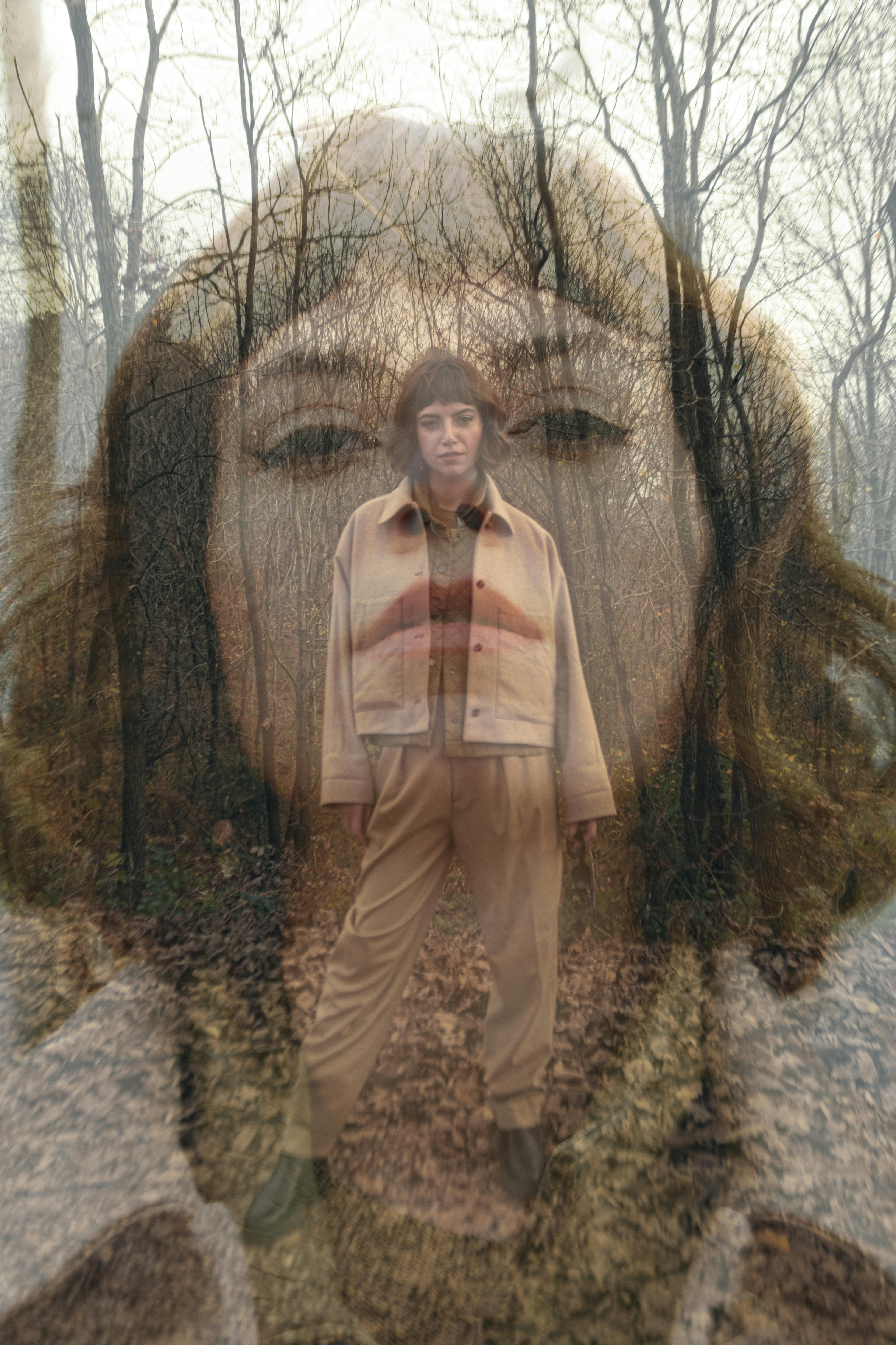 Artistic double exposure of a woman in a forest during fall creating a surreal effect.
