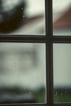 Close-up of a window with water droplets on a rainy day, creating a moody atmosphere.