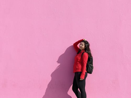 Подросток с рюкзаком позирует на фоне розовой стены