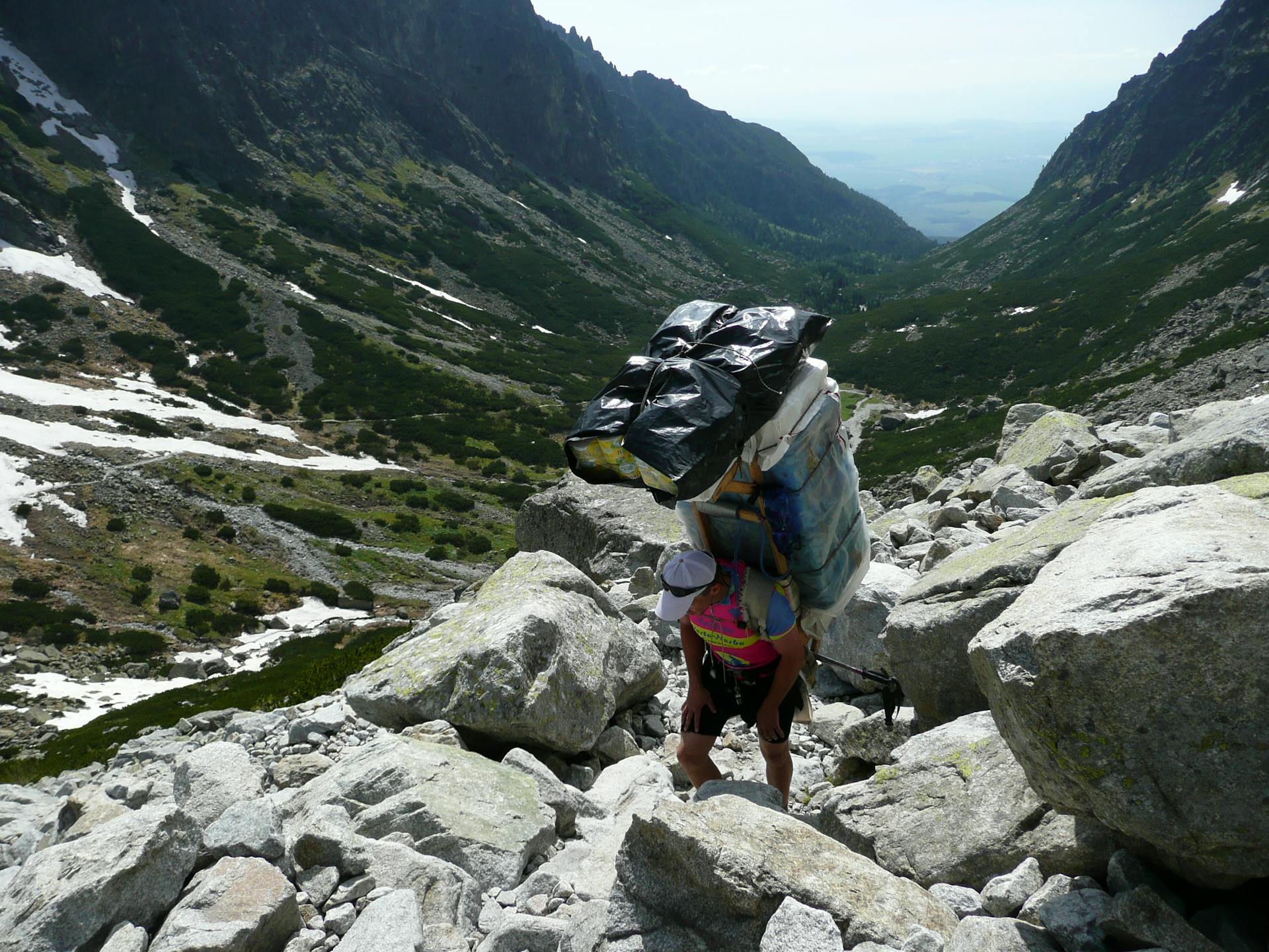 Man carrying large load while hiking through rugged mountain valley