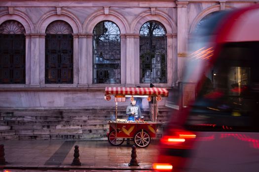 Nighttime street vendor in Istanbul sells traditional snacks with a blurred tram passing by.