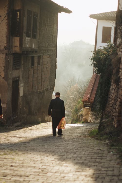 Free A solitary man walks down a cobblestone alley in a misty town, exuding a quiet, reflective atmosphere. Stock Photo
