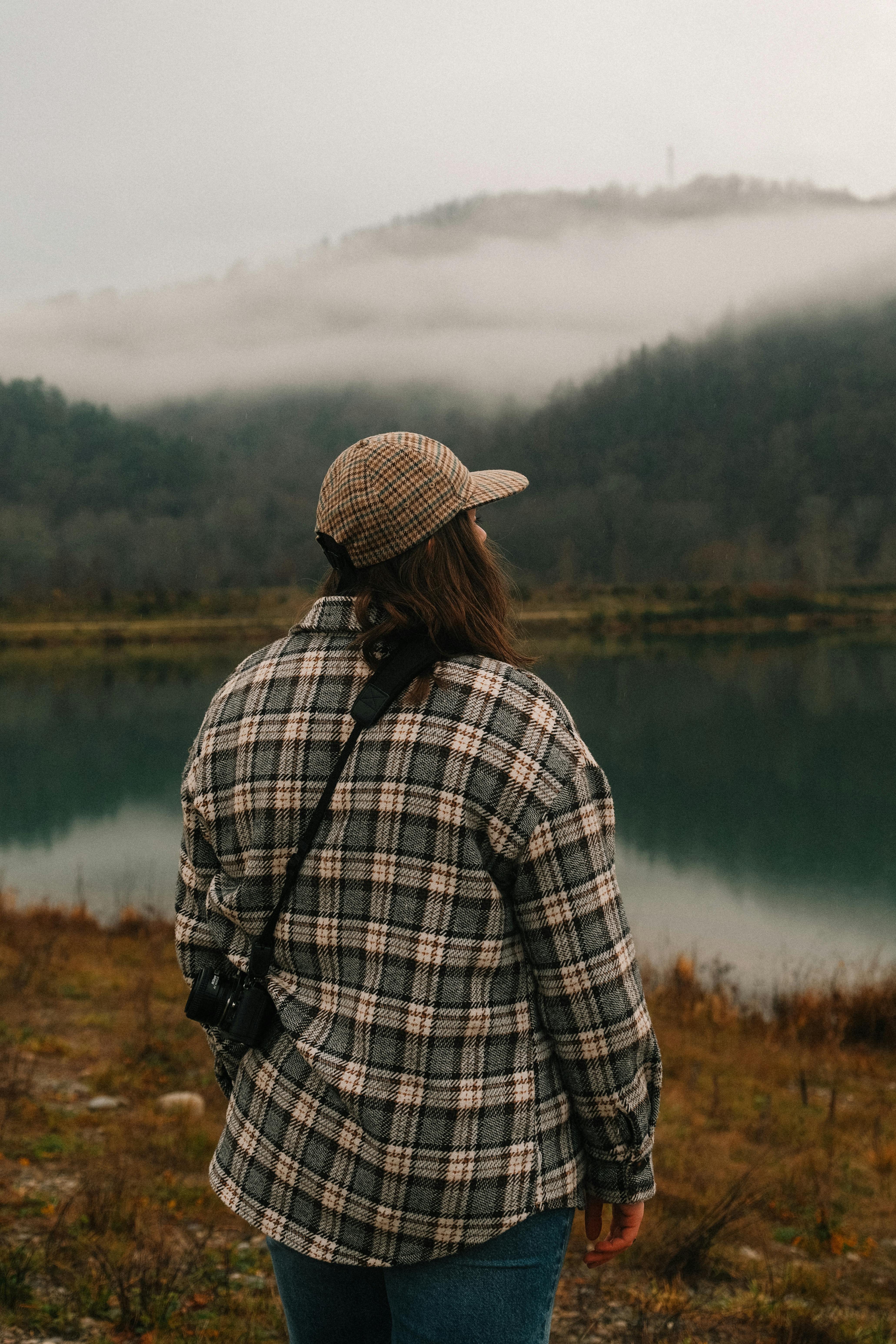 A woman contemplates a serene misty mountain lake landscape, embodying solitude and adventure.