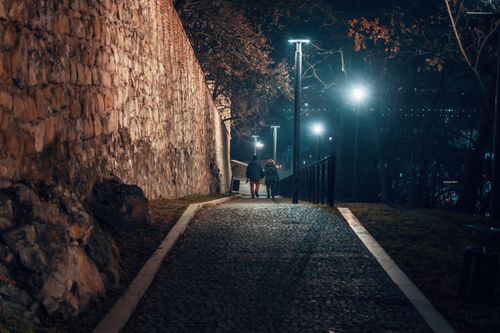 Free Couple walking down a cobblestone street in Bratislava at night with street lamps illuminating the path. Stock Photo