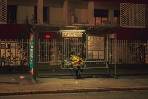 A Person Sitting at a Bus Stop at Night 