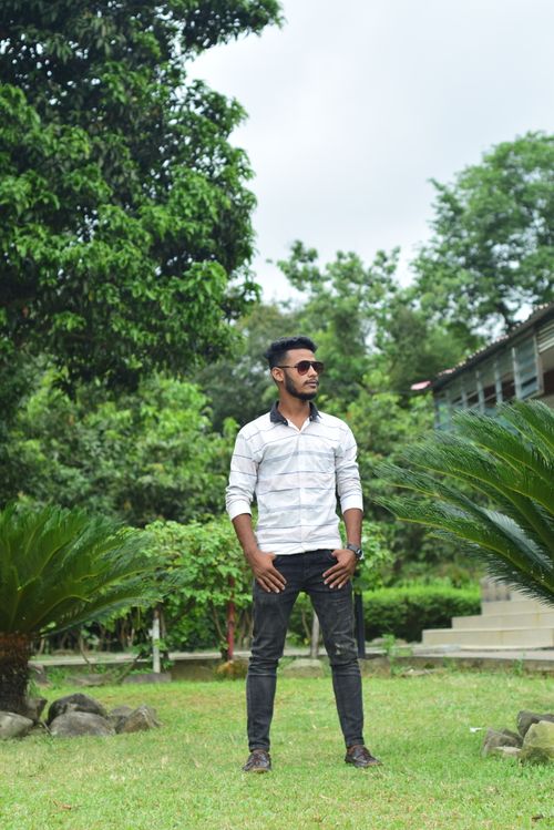 Free Fashionable man posing confidently among lush green foliage in a serene garden. Stock Photo