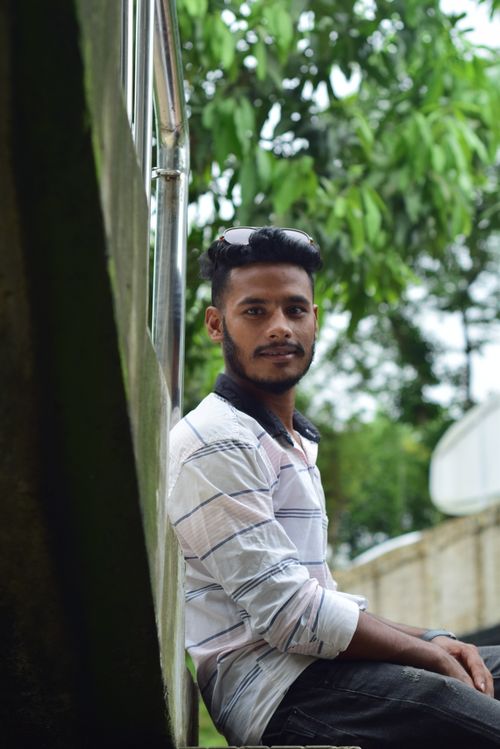 Free A stylish man with a beard in a striped shirt sits outdoors on a ledge. Stock Photo