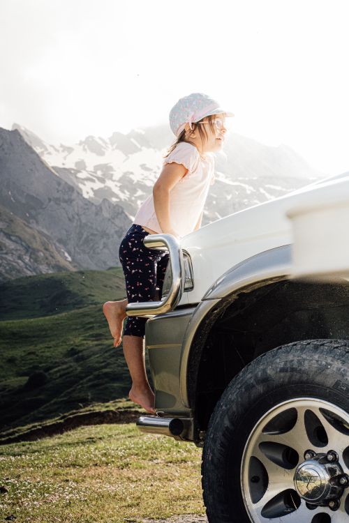 A Little Girl Standing on the Front Bumper of a Car Parked in Mountains ...