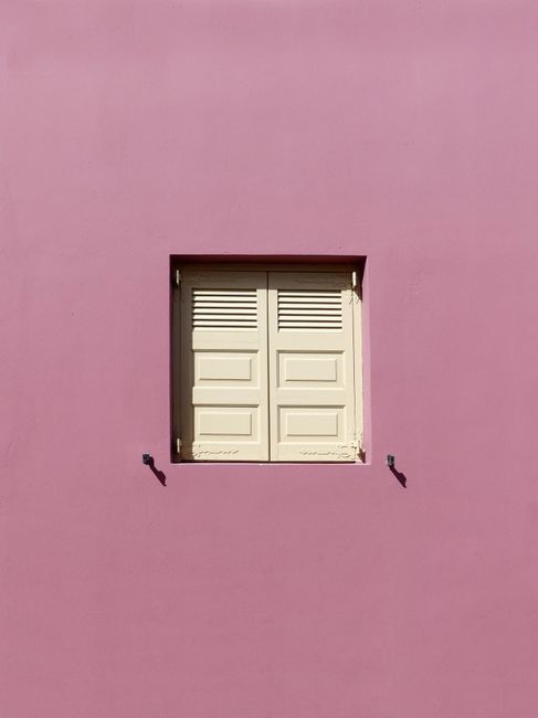Elegant minimalist pink building facade with white shutters in Santorini, Greece.