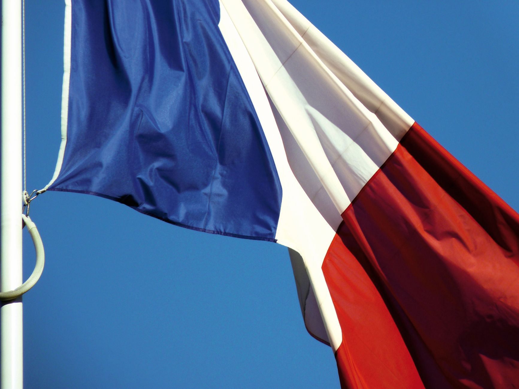 A close-up of the French national flag waving against a clear blue sky in Paris, France.