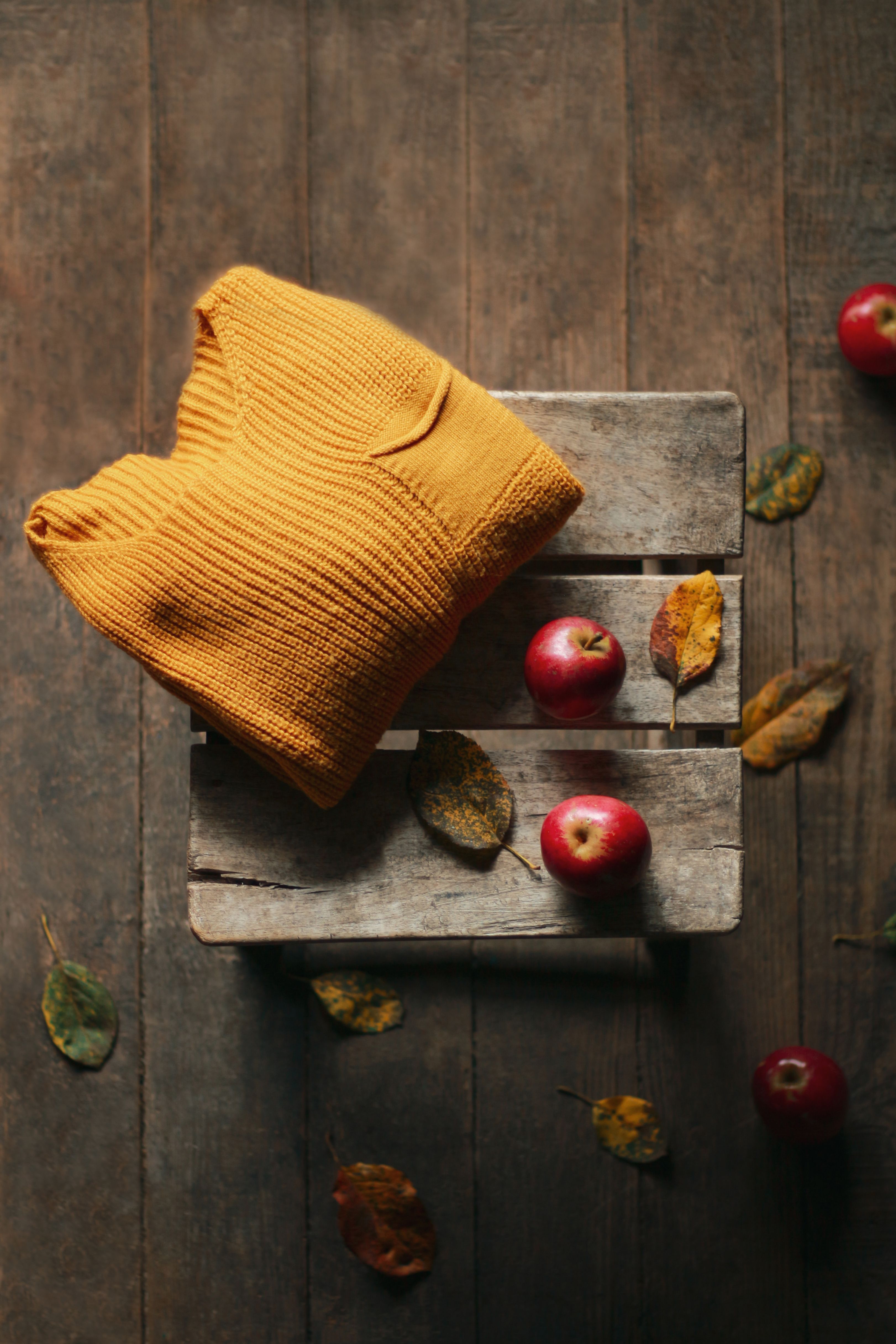 Warm autumn scene featuring a folded mustard sweater and red apples on a rustic wooden crate.