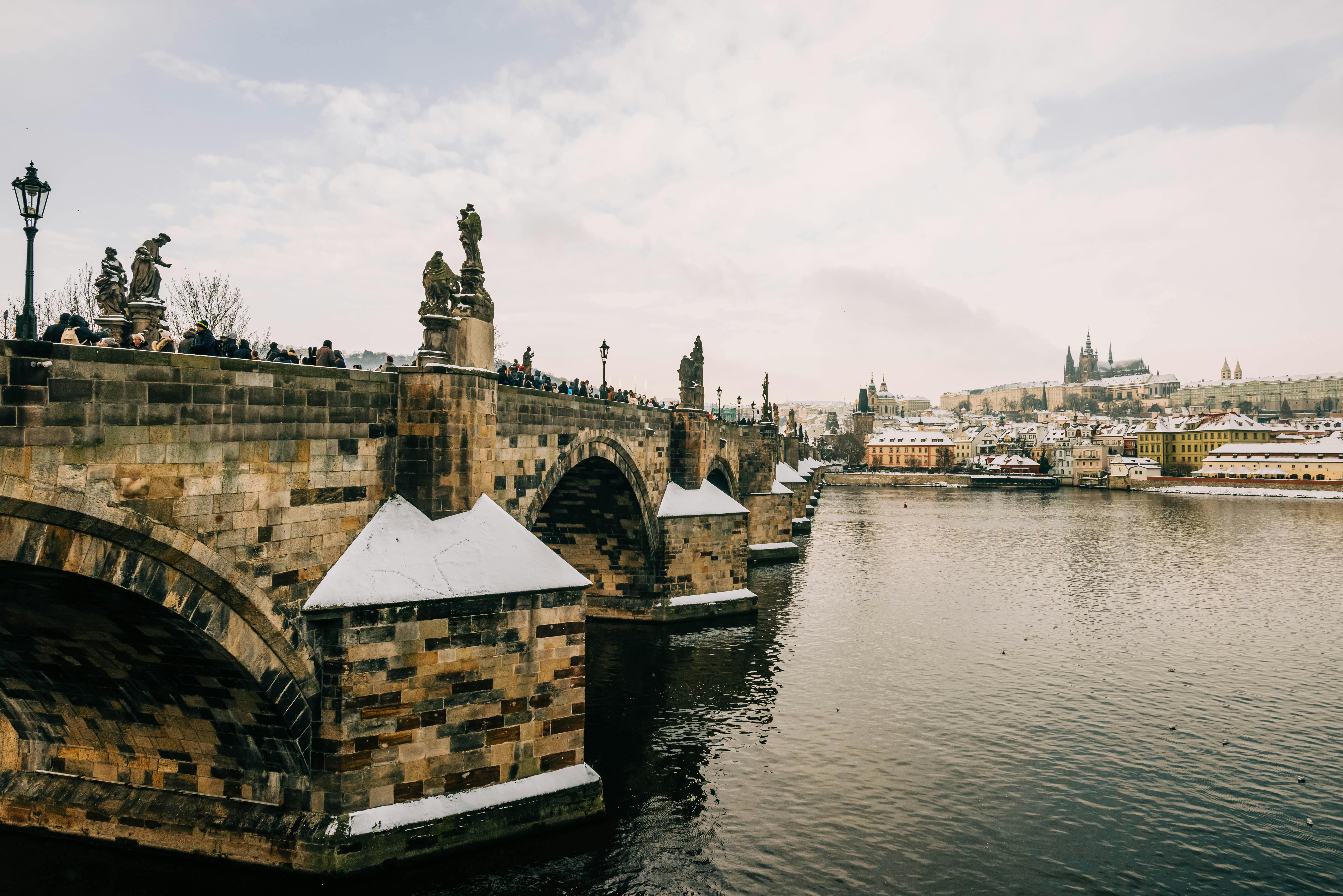 Charming winter scene of the Charles Bridge and river with snowy rooftops in Prague.