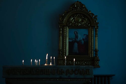 Religious Painting in a Golden Frame and Burning Candles in a Church 