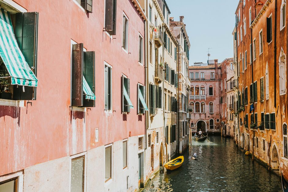 A scenic view of a Venetian canal with gondolas, colorful buildings, and a bright atmosphere.