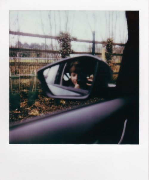 Free A reflection in a car mirror showing a person taking a photo with a fence in the background. Stock Photo