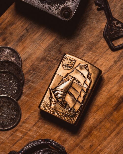 Free Close-up of a vintage brass ship plaque beside coins on a wooden surface, exuding a nautical and rustic charm. Stock Photo