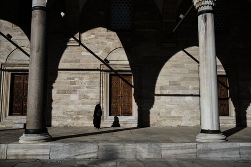 Free A lone woman stands under the dramatic shadows of arches at the Suleymaniye Mosque in Istanbul, Turkey. Stock Photo
