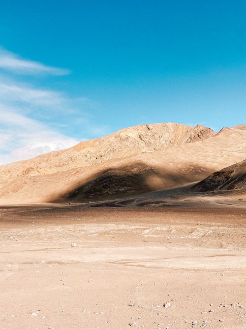 Free A vast desert landscape with mountains under a bright blue sky, featuring soft shadows and sunlight. Stock Photo