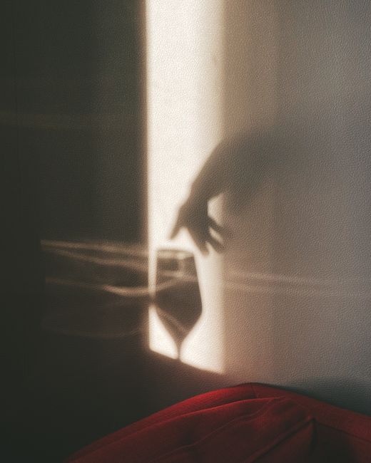 Moody shadow of a hand reaching towards a wine glass, creating a mysterious ambiance.