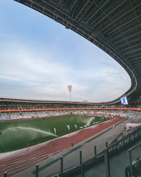 Wide-angle view of a modern stadium in Minsk with sprinklers on the field at dusk.