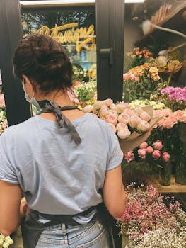 A woman florist in a city flower shop arranges a bouquet of roses amidst an array of colorful blooms.