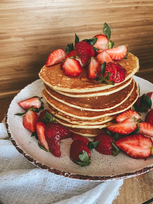 Free Stack of fluffy pancakes topped with fresh strawberries on a white plate, perfect for breakfast. Stock Photo