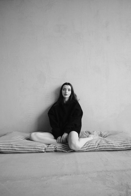Black and white portrait of a woman sitting against a plain wall, capturing a minimalist and moody tone.