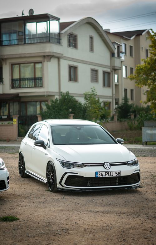 Free A modern white car parked in a quiet residential neighborhood with multi-story buildings. Stock Photo