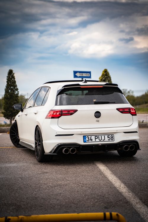 Free White hatchback parked in an outdoor lot under cloudy skies, showcasing rear view with license plate. Stock Photo