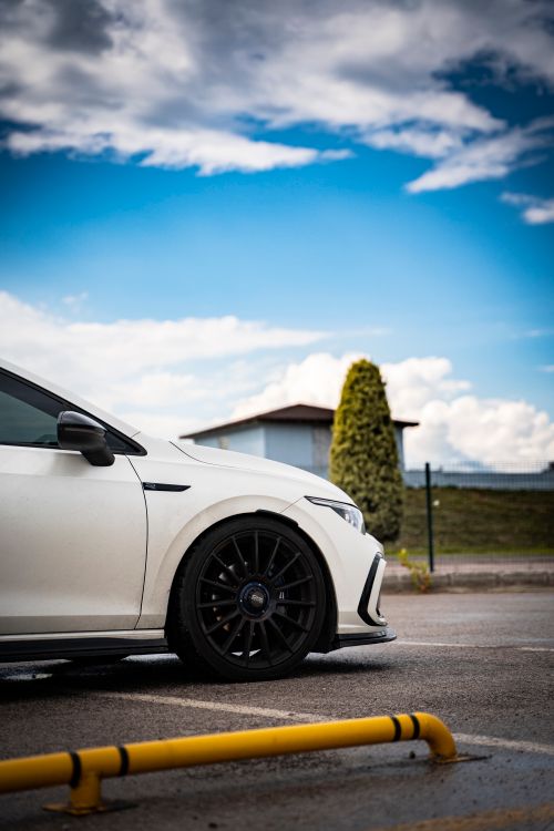 Free A sleek white car parked outdoors with blue skies and urban surroundings, showcasing modern automotive design. Stock Photo