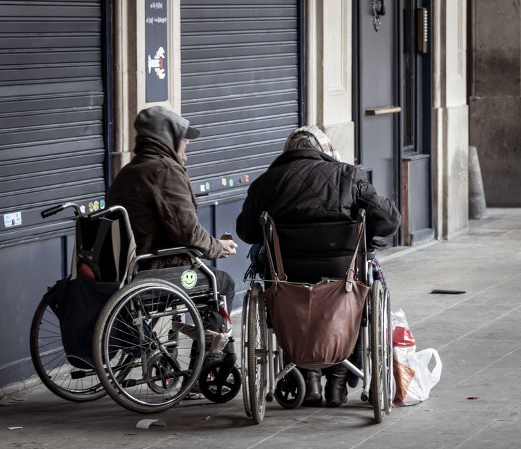 Dos adultos mayores en sillas de ruedas socializando al aire libre con ropa de invierno.