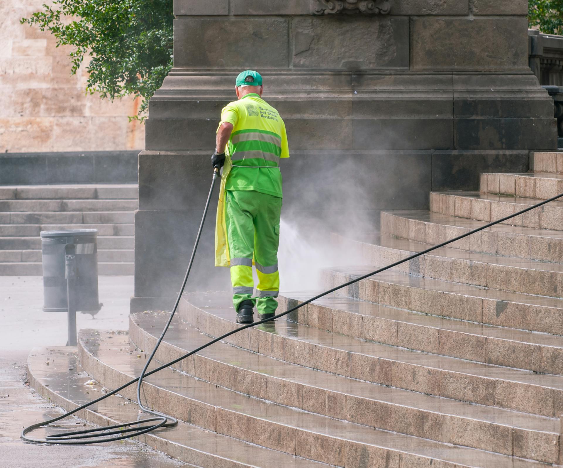 A municipal worker power washing stone steps outdoors, ensuring cleanliness and maintenance.