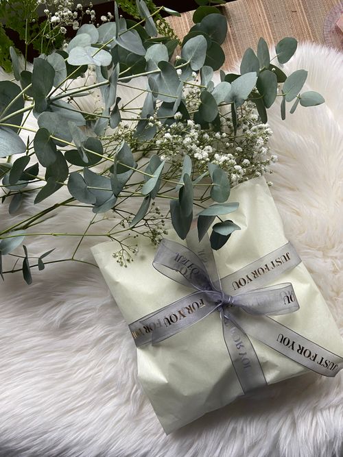 Free Beautifully wrapped gift with eucalyptus leaves and baby's breath on a fluffy surface. Stock Photo